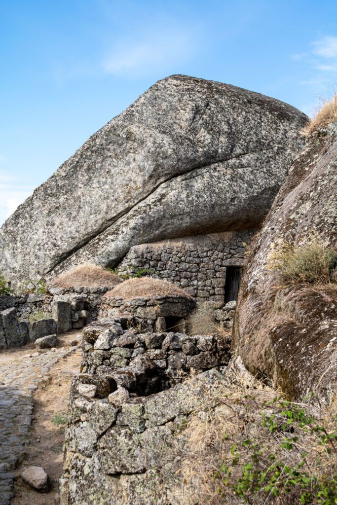 Stone building and walls beneath a large granite boulder in Monsanto, Portugal