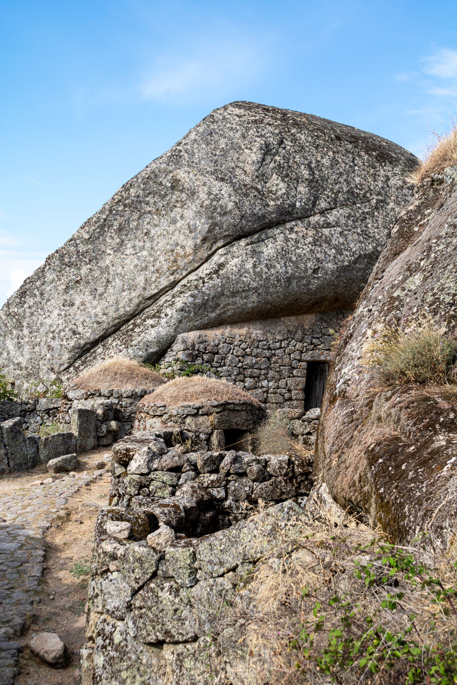 Stone building and walls beneath a large granite boulder in Monsanto, Portugal